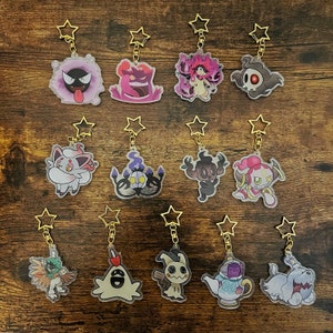 Puede incluir: Colección de llaveros de acrílico transparente con varios diseños de personajes de dibujos animados. Cada llavero tiene un cierre dorado en forma de estrella. Los personajes son de varios colores, incluyendo morado, rosa, blanco y marrón, y se muestran sobre una superficie de madera.