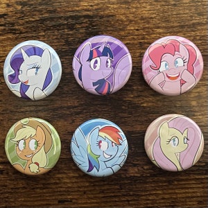 May include: Six round pinback buttons featuring colorful illustrations of My Little Pony characters. Each button has a different pony design, including Rarity, Twilight Sparkle, Pinkie Pie, Applejack, Rainbow Dash, and Fluttershy.