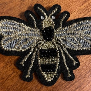 May include: A black felt bee applique with gold and silver thread embroidery and black bead accents.