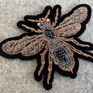 May include: A black velvet embroidered bee with gold and silver thread and black beads. The bee has a detailed design and is a decorative accent.