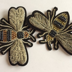 Peut inclure: Deux patchs de broderie en forme d'abeille avec du fil noir, or et argent. Les abeilles ont des corps et des ailes perlés.