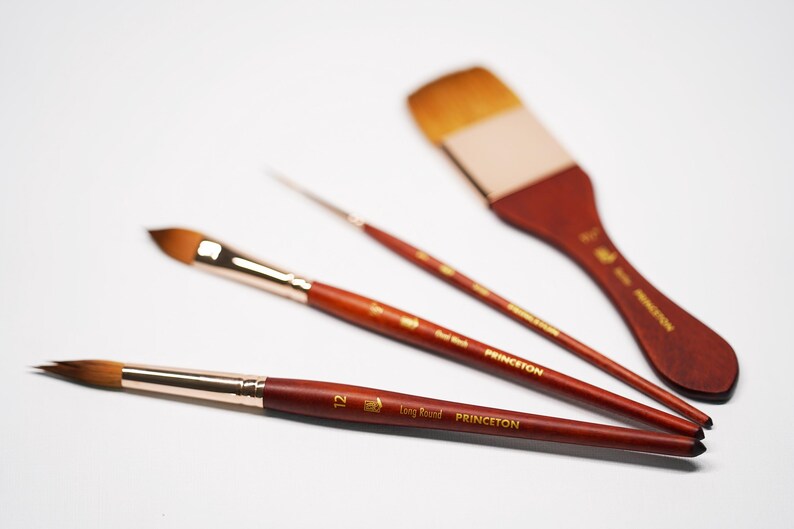 May include: Three paint brushes with wooden handles and gold lettering. The brushes are labeled "Princeton" and "Long Handle". The largest brush has a flat, rectangular head. The other two brushes have round heads.