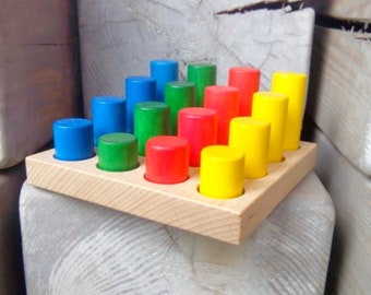May include: A wooden tray with 15 colorful wooden cylinders arranged in a pyramid shape. The cylinders are red, green, blue, and yellow.