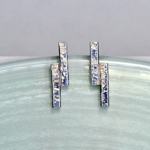 May include: A pair of silver earrings with a textured, geometric design. Each earring features three stacked rectangular bars.