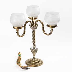 May include: A gold-toned table lamp with three frosted glass shades. The lamp has a twisted stem and a decorative base.