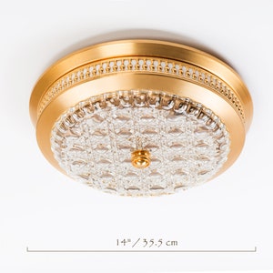 以下が含まれることがあります： クリアなクリスタルガラスのシェードが付いたゴールドの天井照明器具。器具の直径は35.5cmです。