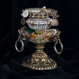 Peut inclure: Un porte-bijoux en métal doré avec un dessus rond et trois pieds. Le support est décoré d'un bol en céramique blanche et de diverses boucles d'oreilles, notamment des perles, de l'argent et de l'or.