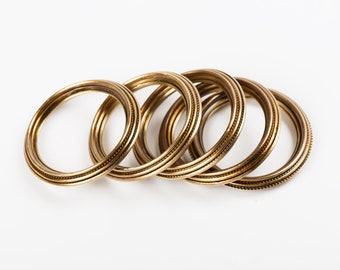 May include: Five gold-colored metal bangles with a textured design. The bangles are stacked on top of each other.