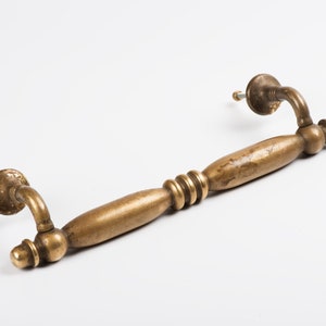 May include: A brass door pull with a rounded, slightly curved design. The pull has a decorative, ribbed section in the centre.