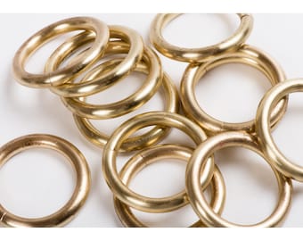 May include: A group of eight brass rings, stacked and overlapping, with a shiny gold finish. The rings are all the same size and shape, and they are arranged in a random pattern.