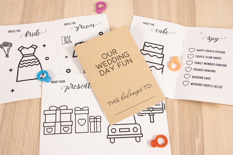 May include: A set of six printable wedding day activity cards with a brown cover that says "Our Wedding Day Fun" and "This belongs to:". The cards include activities like "Dress the Bride", "Dress the Groom", "Wrap Your Present", "Frost the Cake", and "Wedding Day Spy".