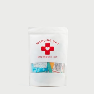 May include: A white, opaque, resealable pouch with a clear window at the bottom. The front features red text that reads WEDDING DAY EMERGENCY KIT, centered above a red cross symbol containing a small white heart in the middle of the cross.