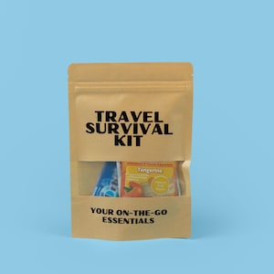 May include: A brown paper travel survival kit with a clear window, containing on-the-go essentials. The kit includes a packet of tangerine-flavored vitamins and electrolytes and a blue item. The text "TRAVEL SURVIVAL KIT" and "YOUR ON-THE-GO ESSENTIALS" are printed on the bag.