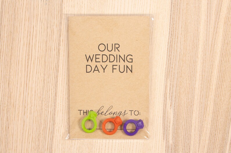 May include: A brown card with the text "OUR WEDDING DAY FUN" and the text "THIS belongs to:" with three colorful ring-shaped objects below the text.