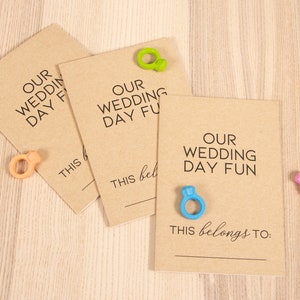 May include: Three brown cards with the text "Our Wedding Day Fun" and a blank line for writing. Each card has a colorful ring attached to it.
