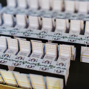 Puede incluir: Disposición de miniaturas de mesa, cada una con una pequeña silla y un diseño de mesa. Las mesas están adornadas con un borde decorativo e incluyen nombres, ideal para una boda o evento.