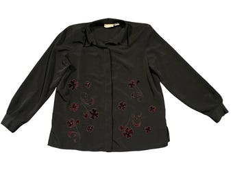 May include: A dark gray long-sleeve blouse with a collared neckline and button-up front. The blouse features embroidered floral designs in a deep red color, adding a touch of elegance to the garment. The sleeves are long and end in buttoned cuffs.