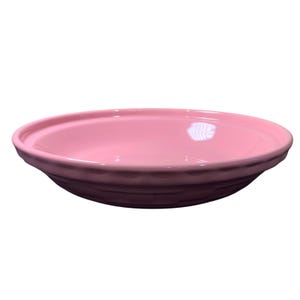 May include: A light pink ceramic bowl with a wide, shallow design. The bowl has a smooth, glossy interior and a textured, ridged exterior. The rim is slightly raised, and the bowl is suitable for serving food.