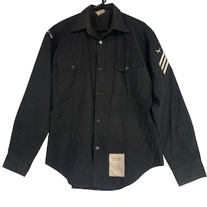 May include: Black long-sleeve shirt with two chest pockets and a collared neckline. The shirt features white stripes and an 'X' on the right sleeve, and text on the left sleeve. A rectangular tag is sewn on the lower front.