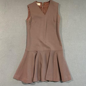 May include: A sleeveless, knee-length dress in a muted mauve color. The dress features a V-neckline and a flared skirt. The fabric appears to be a smooth, possibly knit material. The dress has a simple, classic design.