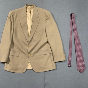May include: A tan blazer with gold buttons and a matching patterned tie. The blazer has two front pockets and a notched lapel. The tie is a deep red with a repeating pattern of small squares. The blazer and tie are displayed on a gray background.