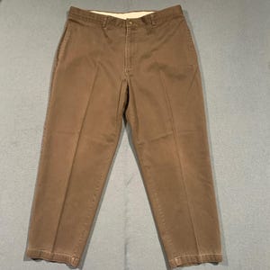 May include: Brown casual pants with a button closure and a straight leg. The pants have a classic design with front pockets and belt loops. The fabric appears to be a durable cotton blend, suitable for everyday wear.