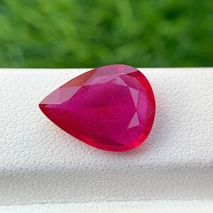 Op de afbeelding: Een levendige roze peervormige edelsteen met een facetgeslepen vorm. De edelsteen is geplaatst tegen een witte achtergrond.