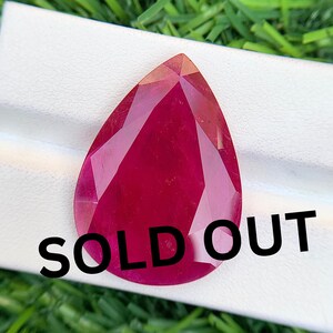 May include: A pear-shaped, faceted gemstone with a deep magenta-red color. The stone features a polished surface with multiple geometric facets that reflect light. The text "SOLD OUT" is printed in bold black letters across the lower portion.