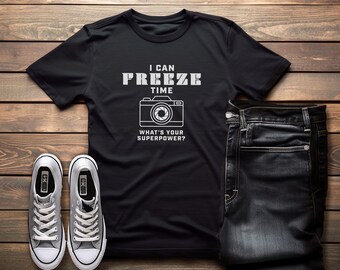 May include: Black t-shirt with the text "I CAN FREEZE TIME" above a camera graphic and the question "WHAT'S YOUR SUPERPOWER?". The shirt is paired with dark wash jeans and gray sneakers with white laces.