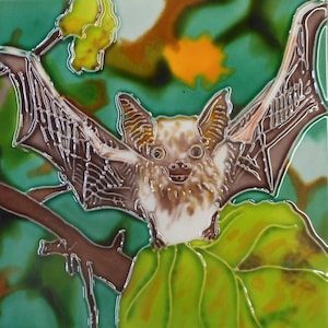 May include: A square ceramic tile featuring a detailed illustration of a bat with outstretched wings. The bat has brown and white fur, with a detailed wing structure. The background is a mix of green, brown, and yellow, depicting foliage.