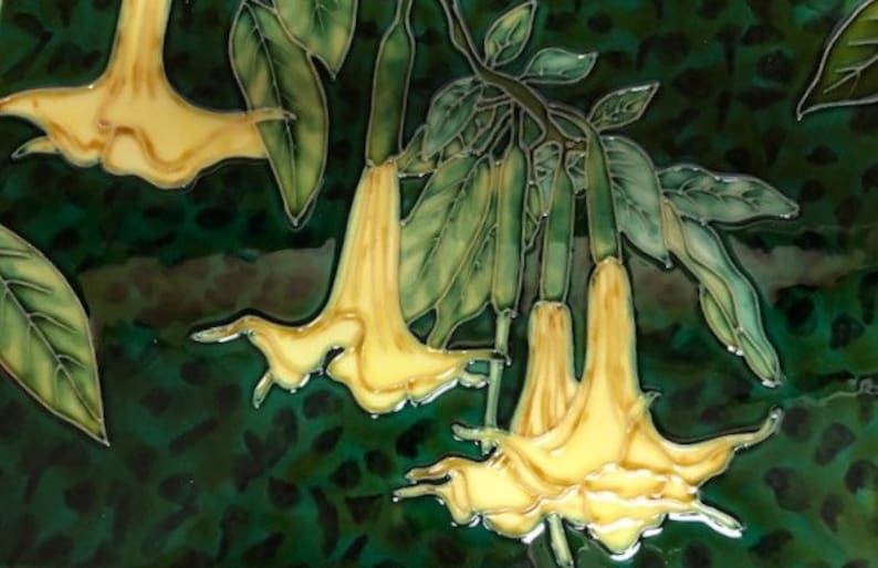 Puede incluir: Un azulejo de cer&aacute;mica con un dise&ntilde;o pintado a mano de flores amarillas de trompeta con hojas verdes sobre un fondo verde oscuro.