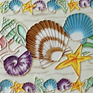 May include: A decorative tile with a seashell theme. The tile features a variety of seashells in different colors and shapes, including a large brown and white seashell, a blue seashell, and a purple seashell. There are also two yellow starfish on the tile.