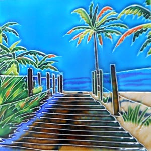 May include: A hand-painted ceramic tile depicting a beach scene with a wooden walkway leading to the ocean. Two palm trees are in the foreground, and the sky is a bright blue.