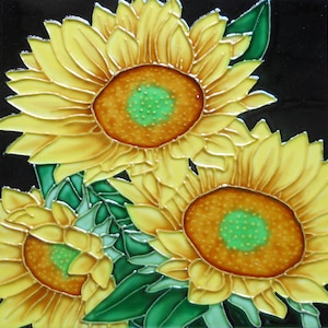 May include: A square ceramic tile with a sunflower design. The sunflowers have bright yellow petals, brown centres with green accents, and green leaves against a black background. The design is detailed with metallic gold outlines.