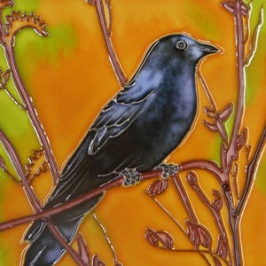 Puede incluir: Azulejo de cerámica con una ilustración detallada de un pájaro azul oscuro posado en una rama. El pájaro se encuentra sobre un fondo naranja y verde vibrante, con ramas y hojas marrones. La obra de arte tiene un acabado brillante.