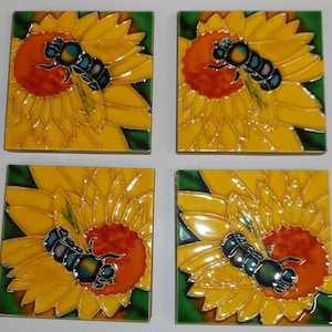 May include: Set of four square ceramic tiles. Each tile features a yellow sunflower with an orange center and a detailed bee. The bee has a black body with blue and green accents. The tiles have a glossy finish and a green border.
