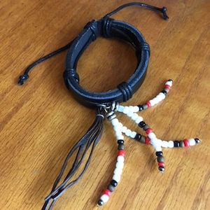 Peut inclure: Un bracelet en cuir noir avec un pompon et des perles blanches, rouges et noires.
