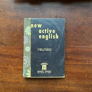 May include: A vintage textbook titled "new active english" with gold lettering on a dark blue cover. The spine is green with a floral pattern. The book is a first edition, revised, published by Editorial Mangold in Madrid.