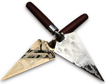 May include: Two gold-colored trowels with wooden handles. The trowels are decorated with Masonic symbols, including a compass, square, and all-seeing eye.