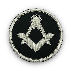 May include: A silver embroidered Masonic symbol on a black velvet background. The symbol is a square and compass with a silver rope border.