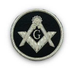 May include: A silver embroidered Masonic emblem on a black velvet background. The emblem features a compass and square with a 'G' in the centre.