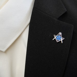 May include: A silver and blue Masonic pin with a square and compass design.