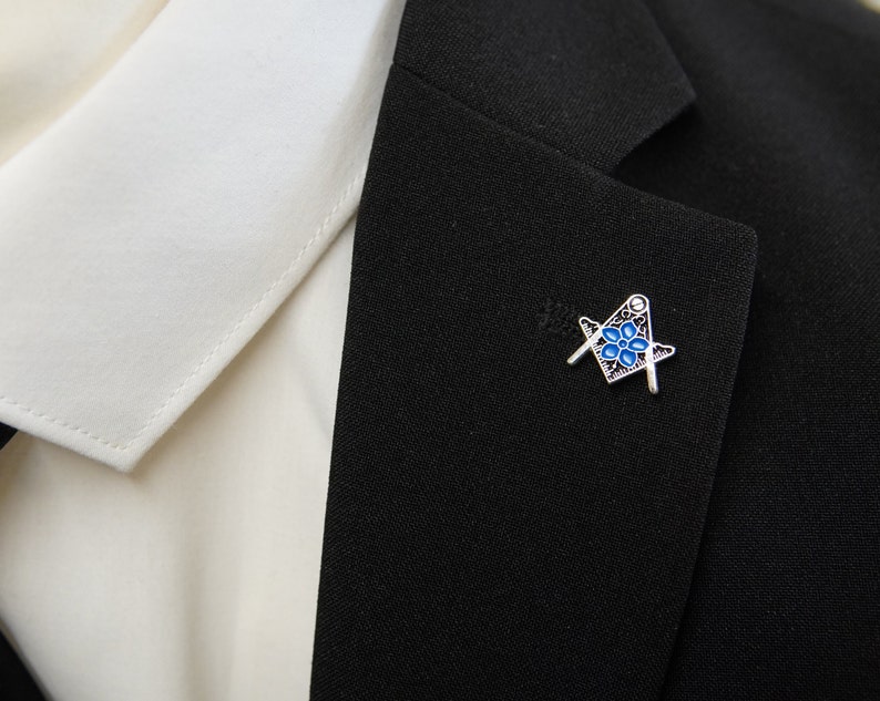 May include: A silver and blue Masonic pin with a square and compass design.