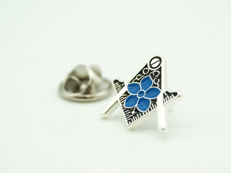 May include: Silver Masonic pin with a blue flower design. The pin has a safety clasp on the back.