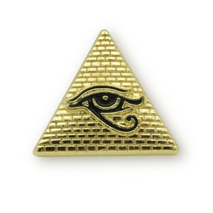May include: A gold-coloured triangular pin with a black and white eye of Horus design. The pin has a textured surface that resembles a pyramid.