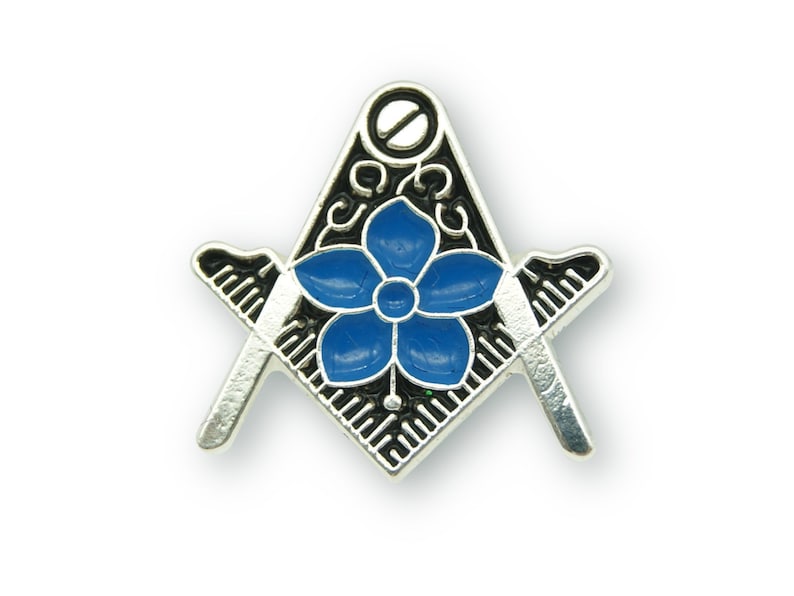 May include: Silver-toned metal pin with a black and white enamel compass and a blue flower in the center.