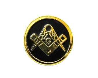 Puede incluir: Pin de metal dorado con fondo de esmalte negro que presenta un símbolo masónico dorado, una escuadra y un compás con una 'G' en el centro.
