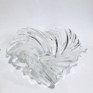 May include: A clear glass bowl with a swirling, wave-like design. The bowl is empty and has a smooth, polished finish.