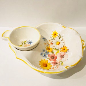 May include: A white ceramic serving dish with a smaller bowl attached. The dish is decorated with a floral pattern of yellow, pink, and blue flowers. The dish has a yellow rim.