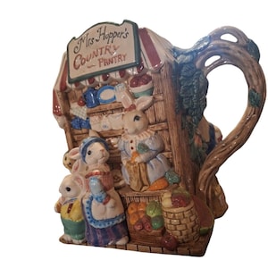 Può includere: Una tazza in ceramica raffigurante una scena stravagante di conigli in una dispensa di campagna. La tazza ha un manico a forma di ramo d'albero ed è decorata con un cartello che recita "Mrs. Hopper's Country Pantry". I conigli sono vestiti con abiti vintage.